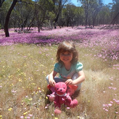 Grace Fulton sits with a stuffed toy in a field of colourful flowers 